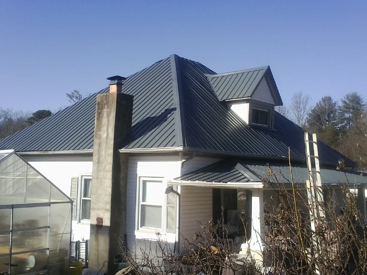 Dark blue standing seam metal roof on a white farmhouse with dormer — Slate & Tile Roof Repair by Roofing Brothers in Owensville