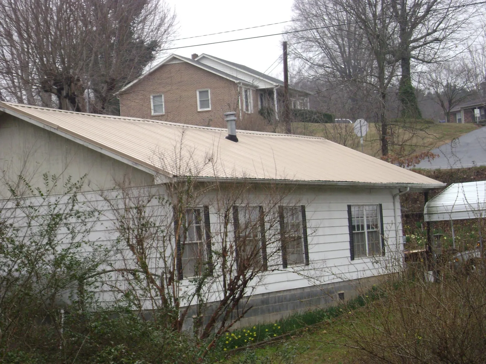 Tan metal roof on a white sided house set into a hillside — Commercial Roofing by Roofing Brothers in Owensville